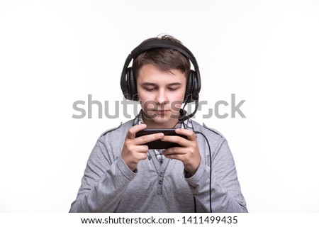 Schoolboy guy teenager with headphones playing a game on mobile phone. Gambling, telephone addiction
