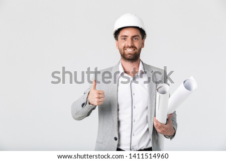 Confident bearded man builder wearing suit and hardhat standing isolated over white background, carrying blueprints, thumbs up Royalty-Free Stock Photo #1411514960