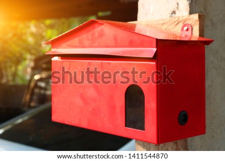 A red steel post box attached to the front post that the sun is shining through.