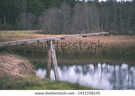 wooden plank bridge over water in forest in autumn with grey colors - vintage old film look