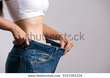 Young slim woman in oversized blue jeans. Fit woman wearing too large pants. Healthcare and woman diet lifestyle concept to reduce belly and shape up healthy stomach muscle. Royalty-Free Stock Photo #1411581224