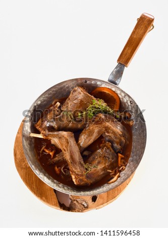 Portions of roasted wild rabbit venison in gravy seasoned with spices, herbs, mushrooms and garnished with orange zest viewed from overhead on a wooden board isolated on white