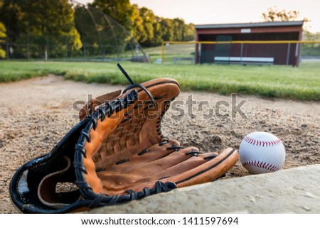 Baseball and glove on pitcher's mound near dugout in early morning 