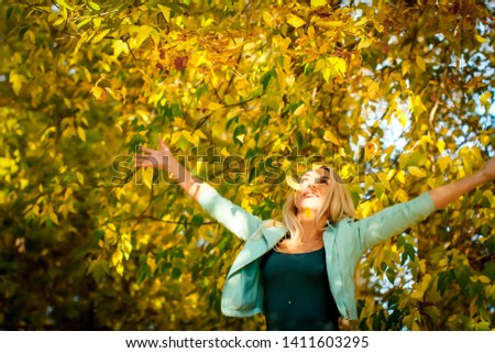 Happy woman throwing up leaves in autumn, smiling. A joyful and excited young woman happily throws yellow leaves in a sunny autumn park. Portrait of a beautiful young woman enjoying autumn in the park
