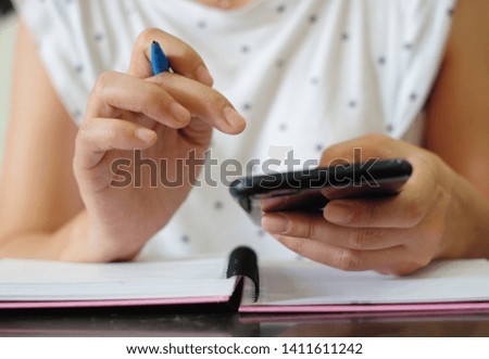 Woman's hand is pressing the phone and writing notebook.