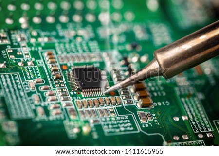 Soldering a micro chip processor with iron tool on a green circuit boad. Electroncs service technology and macro computer concept background. Royalty-Free Stock Photo #1411615955