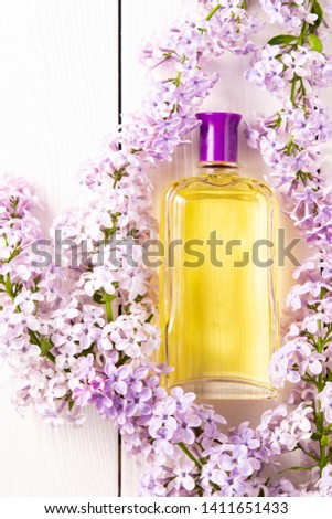 yellow bottle of women's perfume with lilac flowers on white wooden background