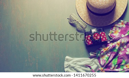 Summer holiday theme preparation checklist - Straw boater hat with black ribbon, plastic heart shaped glasses, toy camera, white camisole, colorful Hawaiian shirt on green background. (vintage filter)