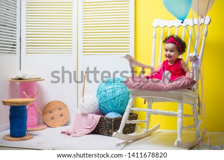 Happy smiling sweet baby girl sitting on armchair with birthday balloons	