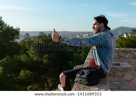 Young man with cap takes a picture with the city in the background. Lifestyle concept.