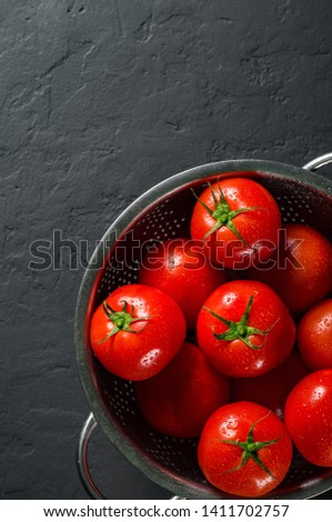raw whole washed cherry tomatoes in a colander on Dark grey black slate background with copy space. top view