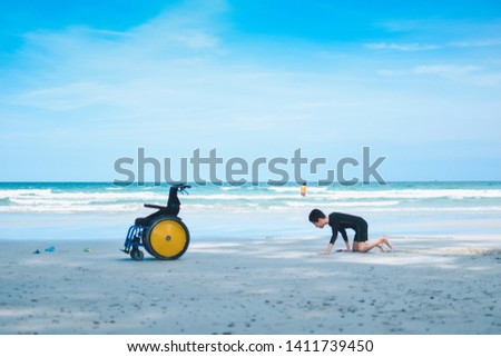 The beautiful beach and disabled child crawling on to his wheelchair, Softly focus, Life in the education age of special Children, Happy disabled kid concept.