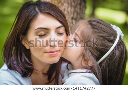 Adorable four years old cute little girl kisses her mother with love.Happy family on a summer meadow. little girl child baby daughter hugging and kissing mother 