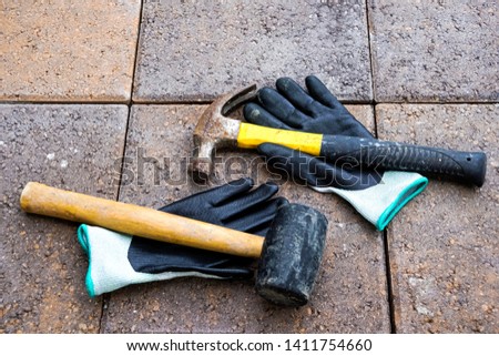 Black gloves under Yellow Hammer and Mallet on road paving stone.