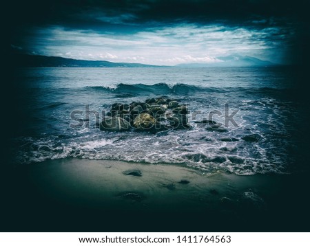 Sea wave on the sand beach with vignette effect frame. Beach landscape view with rocks in the sea.