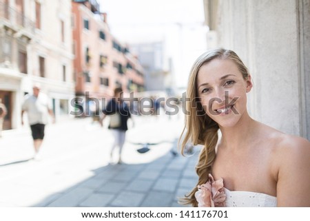 Head and shoulders portrait of a beautiful smiling woman in a city street with high key background and blurred pedestrians