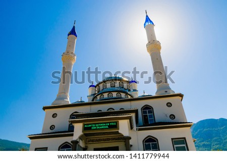 Sun behind the minaret of a Mosque displaying a message in Turkish "The most high religion in Allah is Islam"