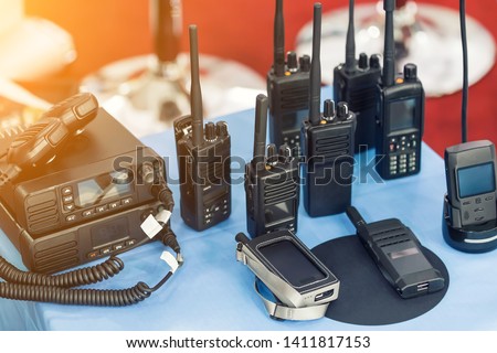 Many portable radio transceivers on table at technology exhibition. Different walkie-talkie radio set. Communication devices choice for military and civil use Royalty-Free Stock Photo #1411817153