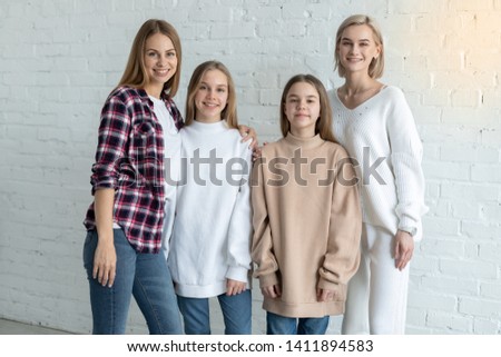 Portrait of beautiful lesbian family in casual clothes, two mom's and daughters smiling looking at the camera against white wall background