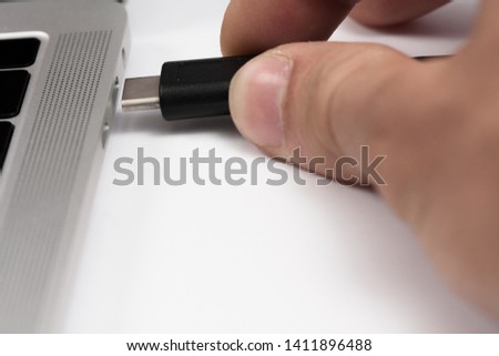 Person inserting the USB cable into the laptop, close-up of the photo, with a white background.