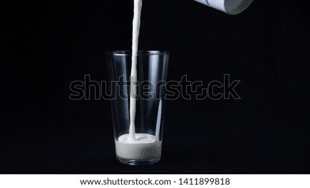 Slow motion of delicious milkshake with ice cream filling the clear glass on the black background. Frame. Cocktails with milk and ice cream