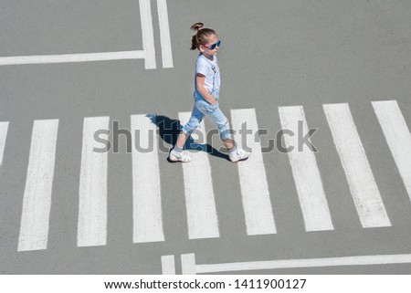 In the summer on the street at the pedestrian crossing kid girl in fashion clothes cross the road. From top view. Shadow at zebra crossing