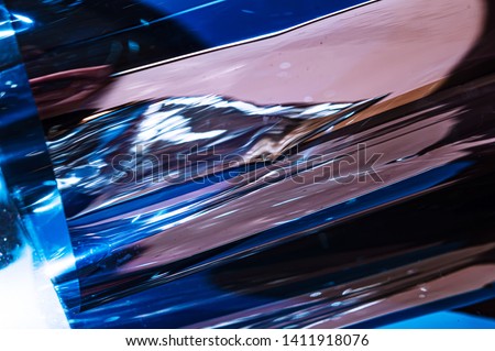 Holographic plastic wrinkled film with contrast sun light reflections. Blue tones with dark black shadows on metallic chrome surface. Neon light colors. Abstract fantasy trendy psychedelic background 