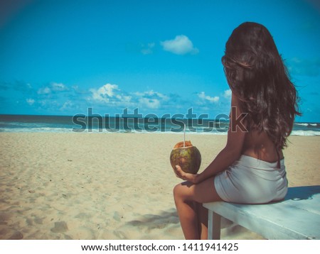 Young woman sitting on the beach holding a coconut