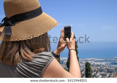 Woman tourist wearing hat is taking pictures of the Mediterranean Sea in Haifa, Israel