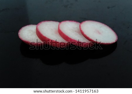 Food photo with sliced ​​and halved radishes on a black dark background. 