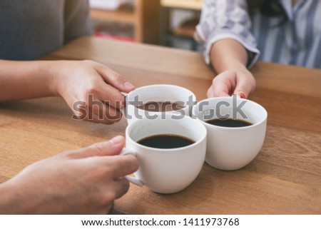 Closeup image of three people holding and clinking coffee cups to drink on wooden table