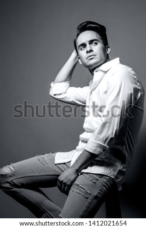 Black&white portrait of a handsome young man in white shirt and jeans posing against gray background. Studio shot.