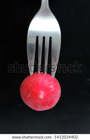 Food photo with sliced ​​radish on a fork on a black dark background.