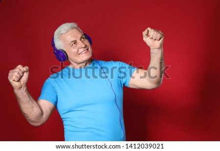 Mature man enjoying music in headphones on color background