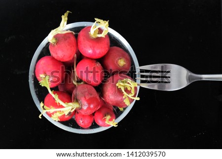 Food photo with radish in a glass bowl with fork on a black dark background. Top view
