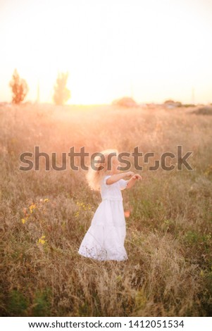Cute little girl with blond  hair in a summer field at sunset with a white dress
