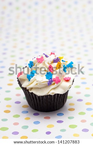Close-up image of cupcake with colorful floral pattern sprinkles over polka dots background.