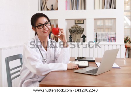  Young woman doctor holding a red heart, in office.
