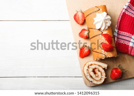 Sweet roll with strawberries and meringues on cutting board on wooden background. Copy space, top view.