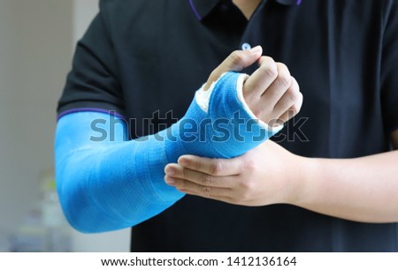 Closeup of asian man's arm with long arm plaster, fiberglass cast therapy cover by blue elastic bandage after sport accident. Appropriate treatment in western medicine. Royalty-Free Stock Photo #1412136164