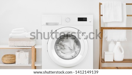 Washing machine with laundry and shelves on white wall background Royalty-Free Stock Photo #1412149139