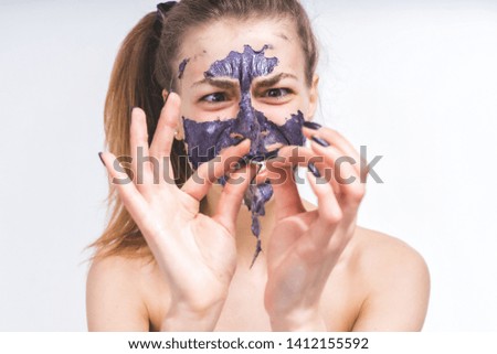 Removal of a cosmetic mask from the face of a beautiful young girl. Torn to pieces. An interesting picture on an empty background.