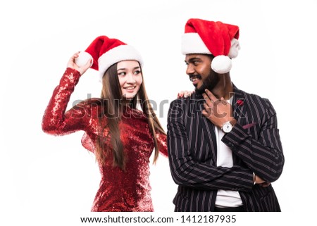 Portrait of a cheerful asian couple in christmas hats hugging and looking at camera isolated over white background
