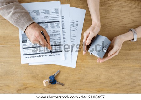 top view of man holding pen near new house loan application form and woman with house model in hands 