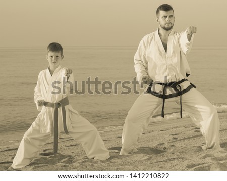 Male coach and boy in karate uniform training at sunny sea beach