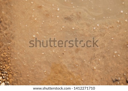 Brown surface of the water in the puddle and the drops and bubbles on it