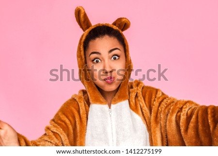 Young woman in bunny kigurumi standing isolated on pink background hands open taking selfie photo on smartphone looking camera pouting lips close-up