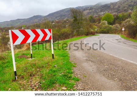 Dangerous turn, red and white striped arrow. Road sign mounted on a roadside of a mountain road