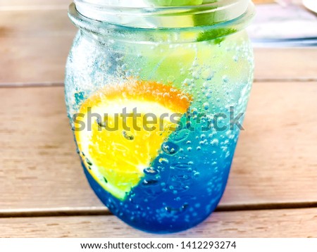 Cold blue colored juice served with orange slices and mint leaf on wooden table. Cold drink for summer.