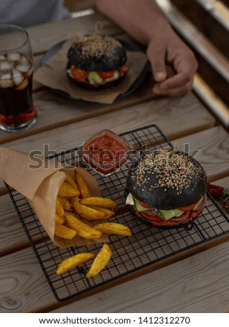 black burger with potato wedges and sauce top view